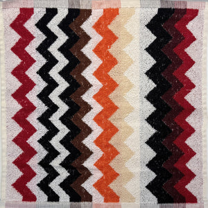 Textile with zigzag pattern in red, black, white, and beige on a checkered fabric background